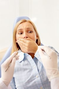 Young woman in dentist chair suffering from dental anxiety.